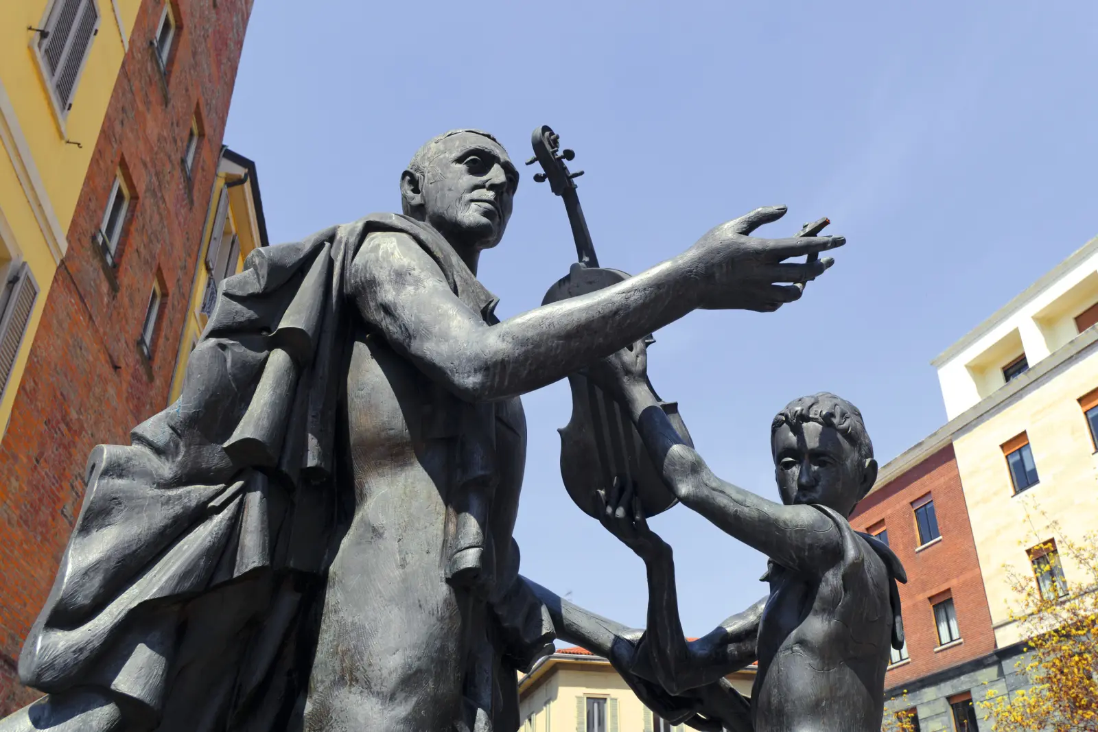 Statue en bronze d’un homme et d’un enfant avec un violon devant des bâtiments.