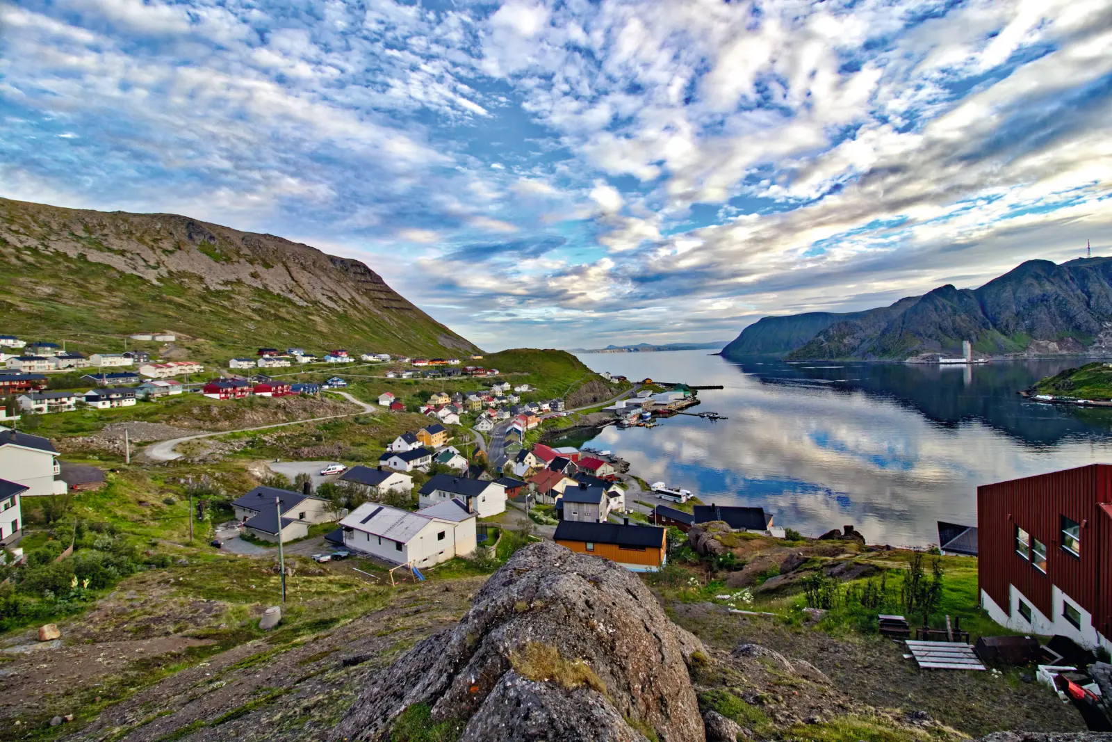 Coastal village with colourful houses, mountains and water in the background under a cloudy sky.
