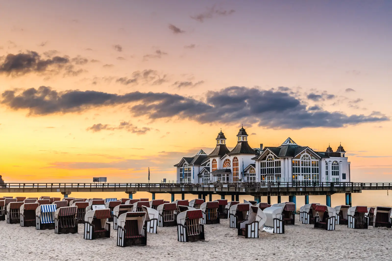 Jetée au coucher du soleil avec des chaises de plage au premier plan.