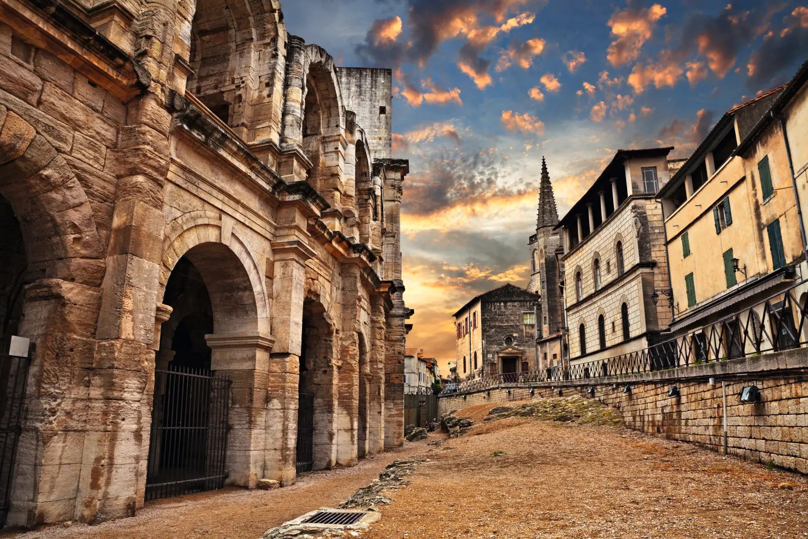 Roman amphitheatre at sunset with historic buildings.