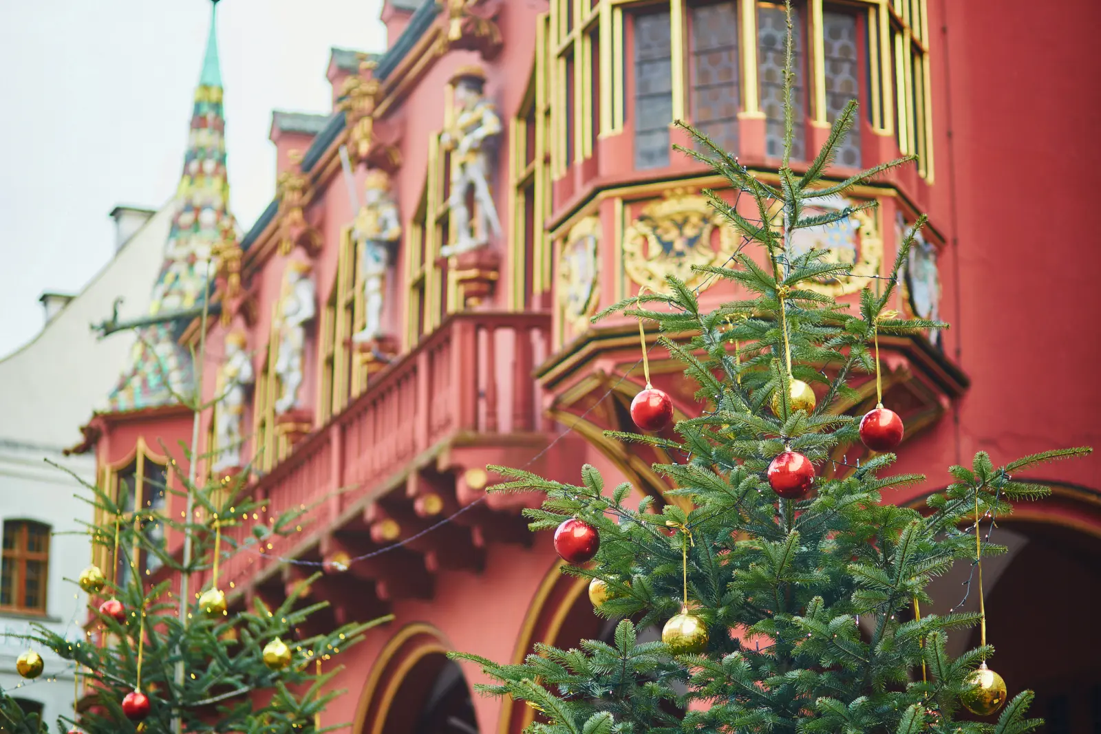 Two Christmas trees in front of a red, ornate building.