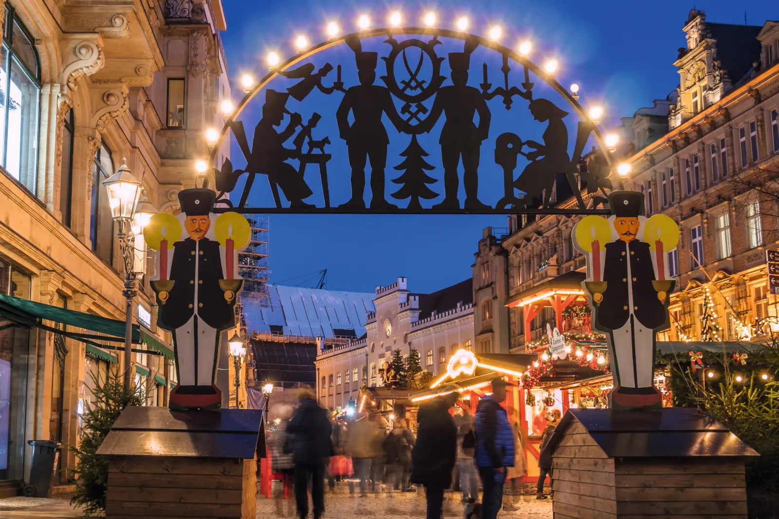 Ingresso di un mercatino di Natale con arco luminoso tradizionale (Schwibbogen) e persone.