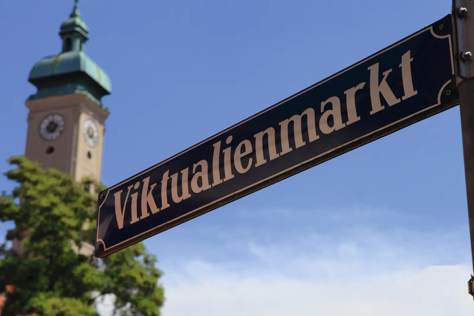 Panneau indiquant Viktualienmarkt devant un clocher d’église.