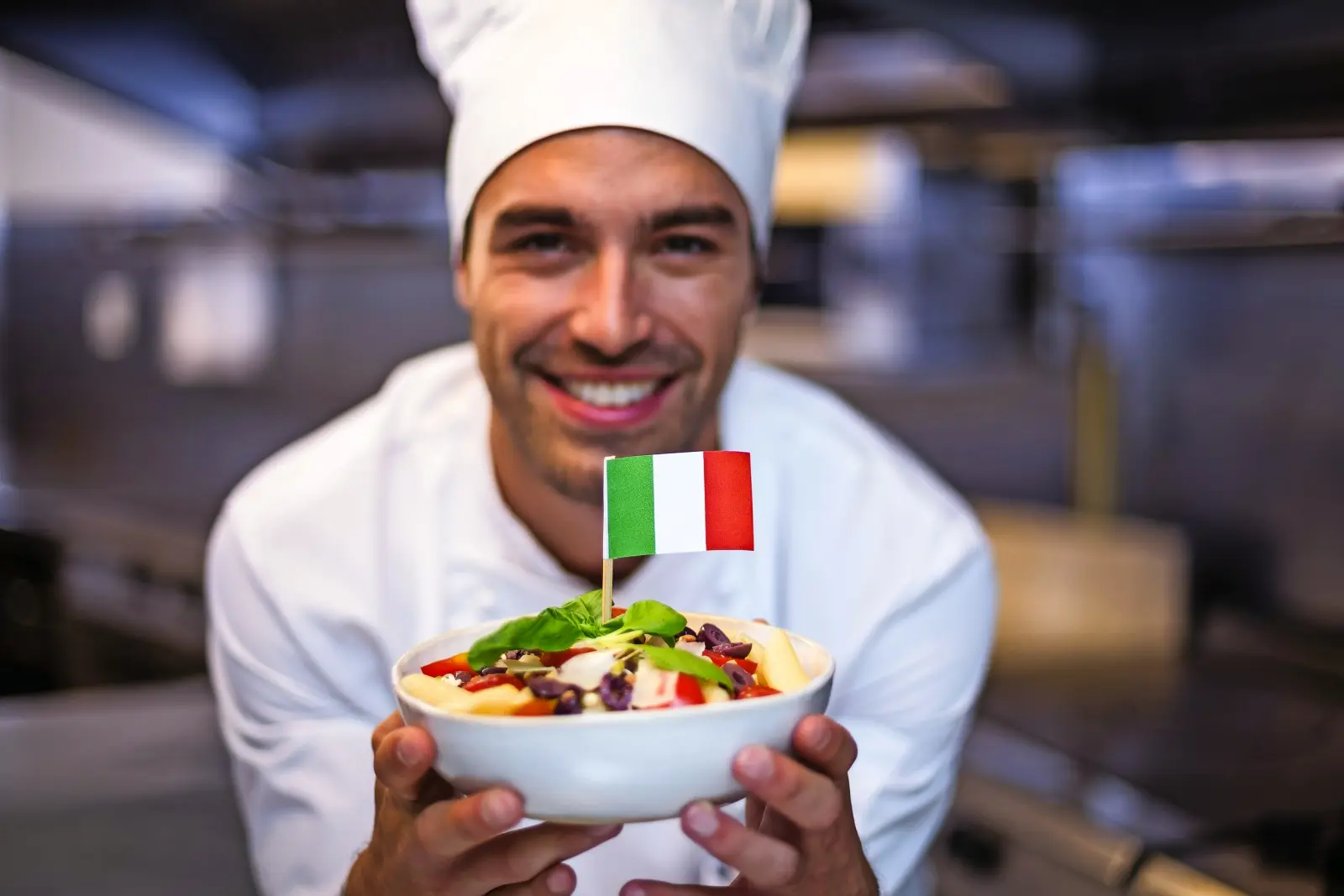 Cuisinier en tenue blanche tenant des pâtes avec le drapeau italien.
