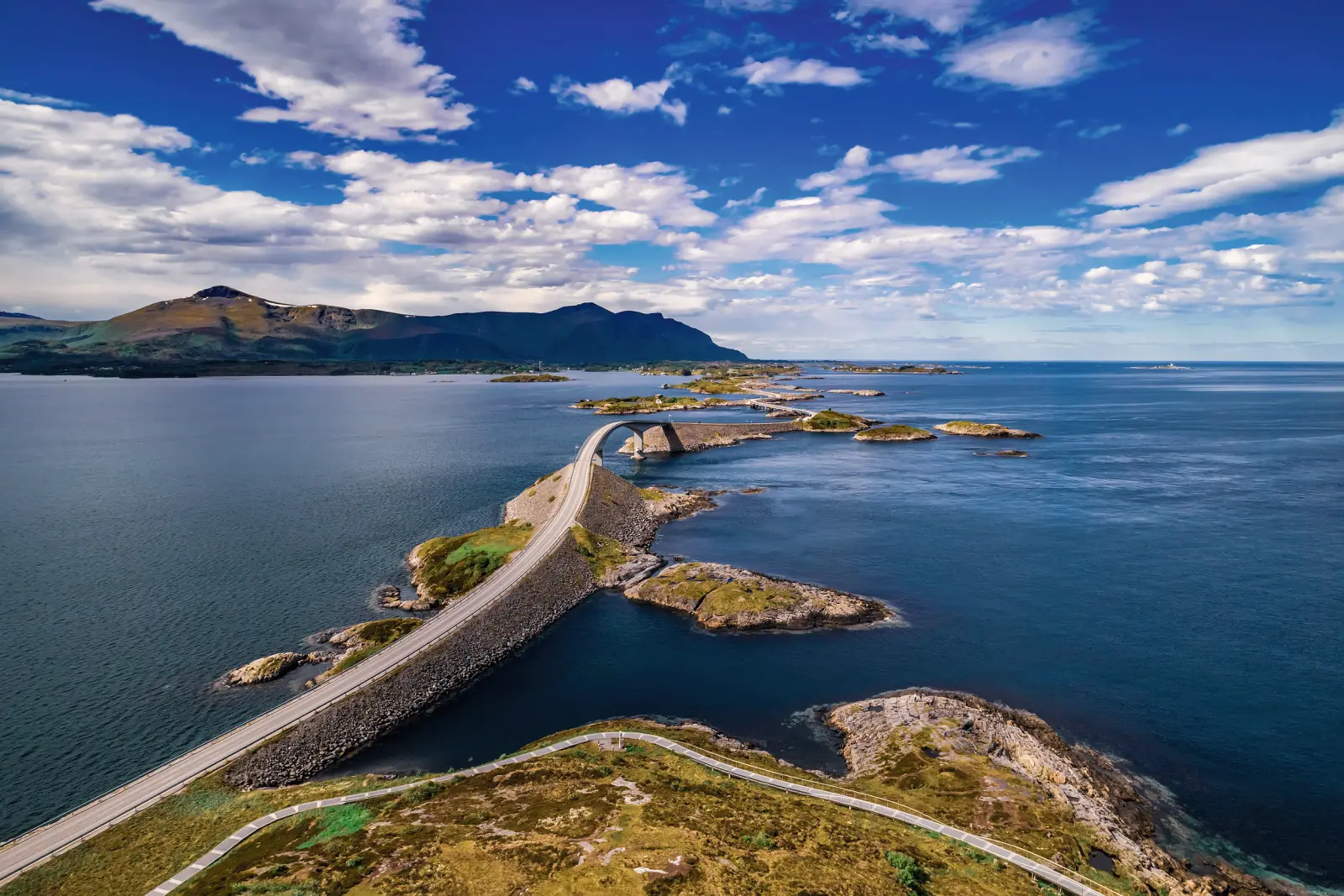 Bridge over the sea with mountains and blue sky in the background