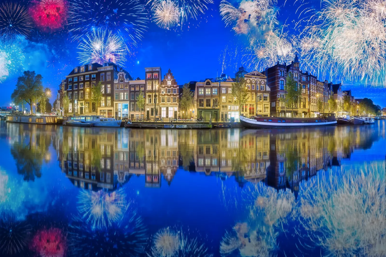 Feux d’artifice au-dessus des canaux illuminés d’Amsterdam de nuit.