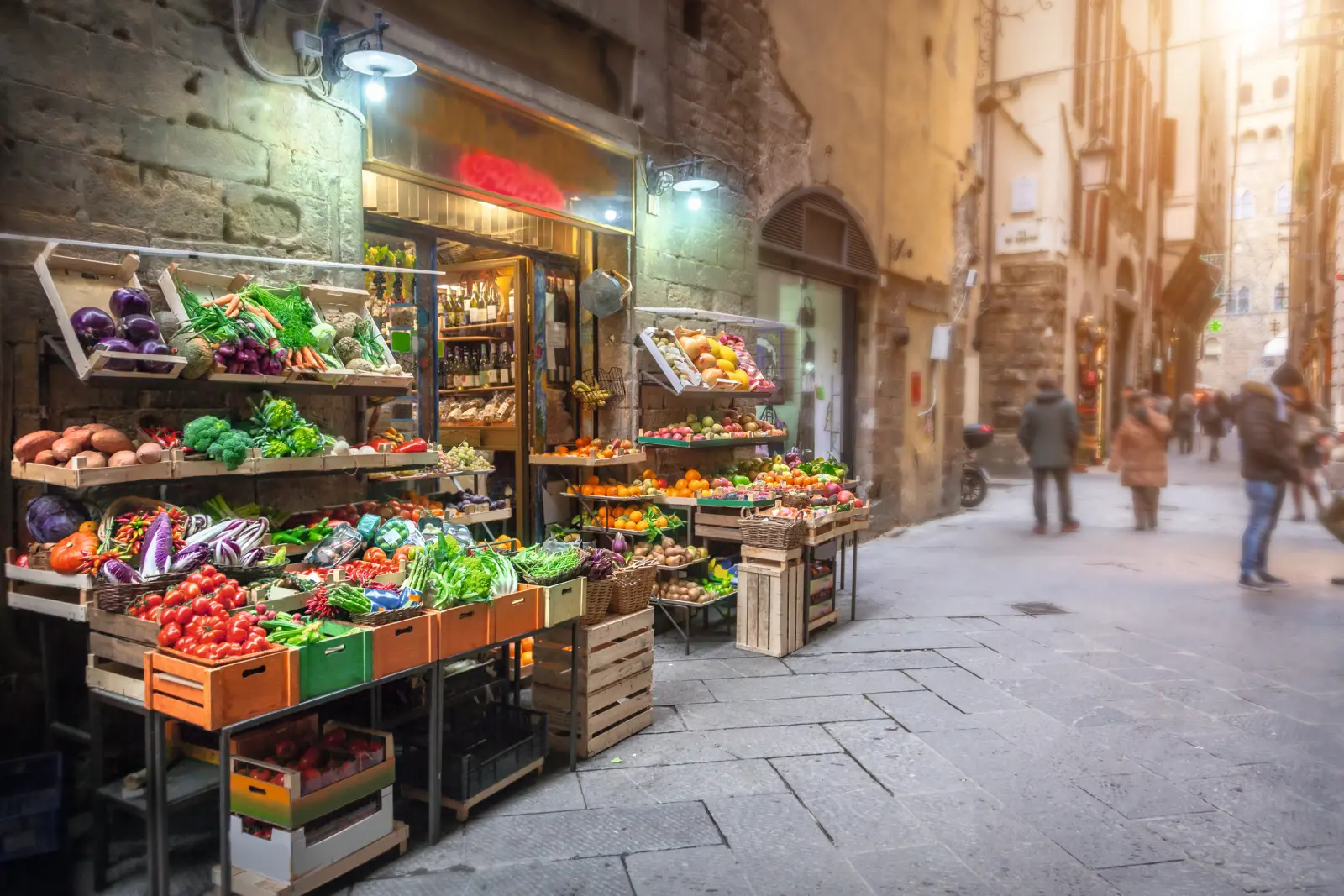 Gemüsestand in einer engen, gepflasterten Gasse einer Stadt.