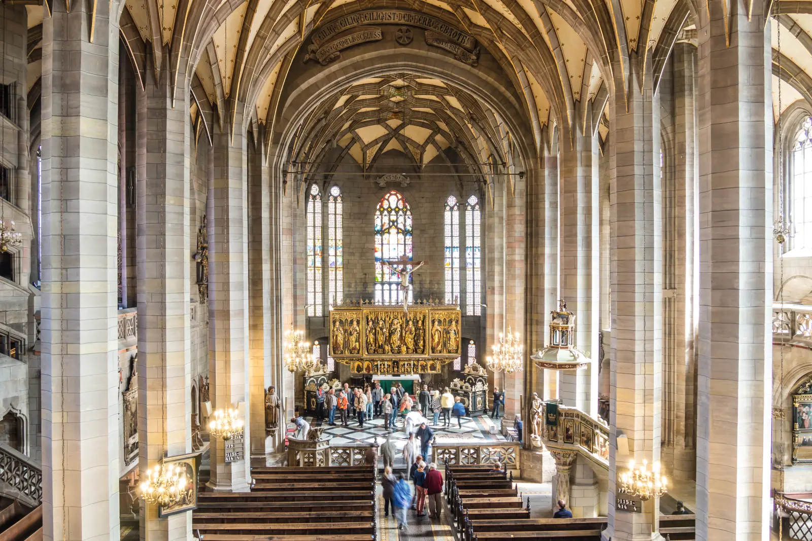 Interno di una chiesa gotica con vetrate colorate e visitatori.