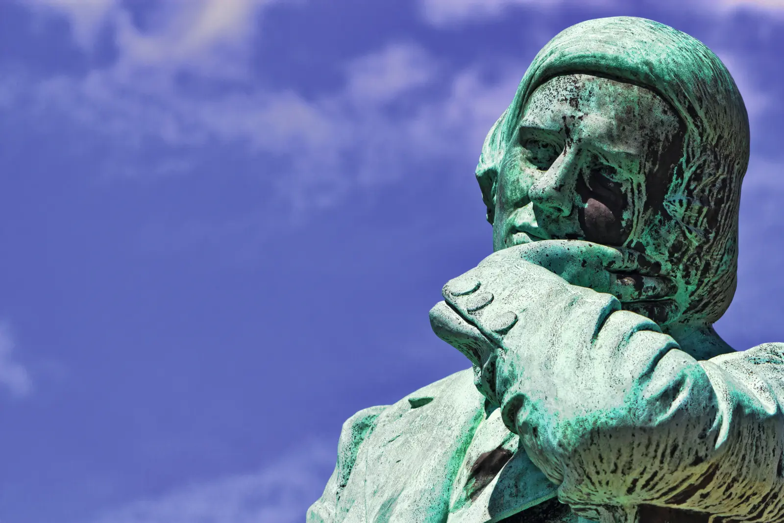 Statua verde in bronzo di un uomo pensieroso davanti a un cielo azzurro.