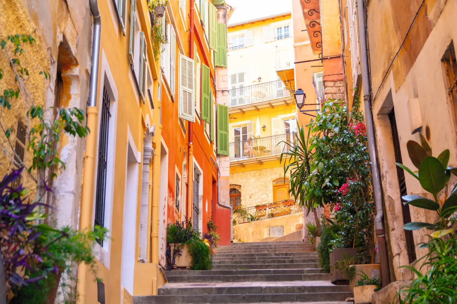 Maisons colorées dans une ruelle étroite et escarpée avec escaliers et plantes.