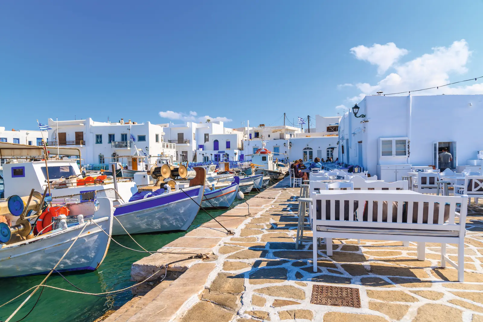 Port avec bâtiments blancs traditionnels et bateaux de pêche sous un ciel bleu.