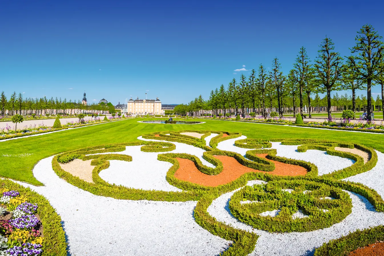 Jardin de château symétrique avec des parterres soignés et des plantes en fleurs.