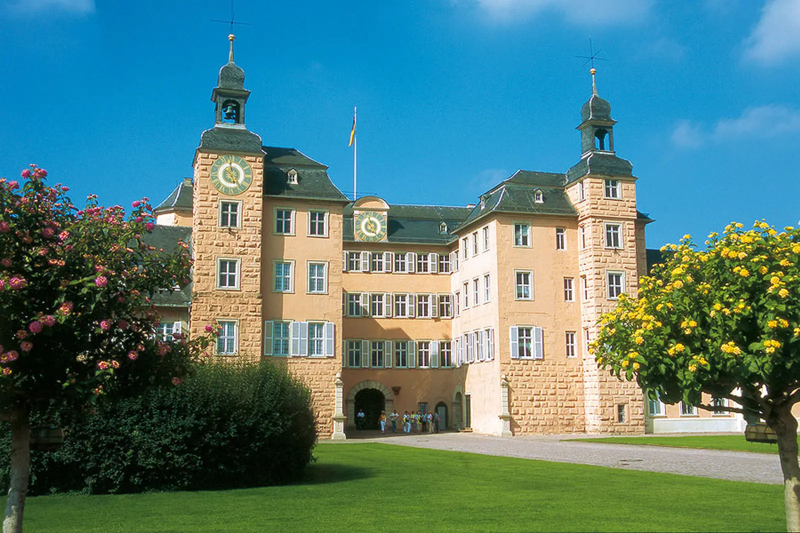Façade du château de Schwetzingen avec ses tours et une pelouse verte au premier plan.