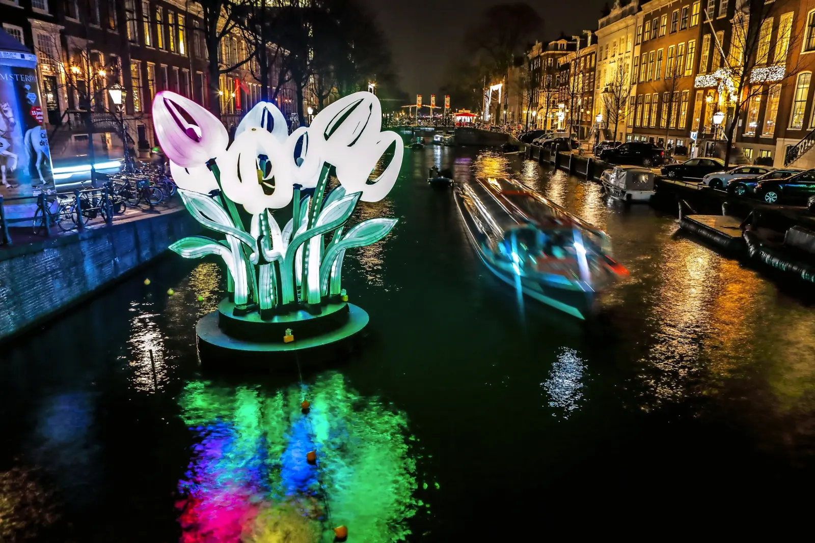 Tulipes lumineuses installées au bord d’un canal de nuit dans une ville.