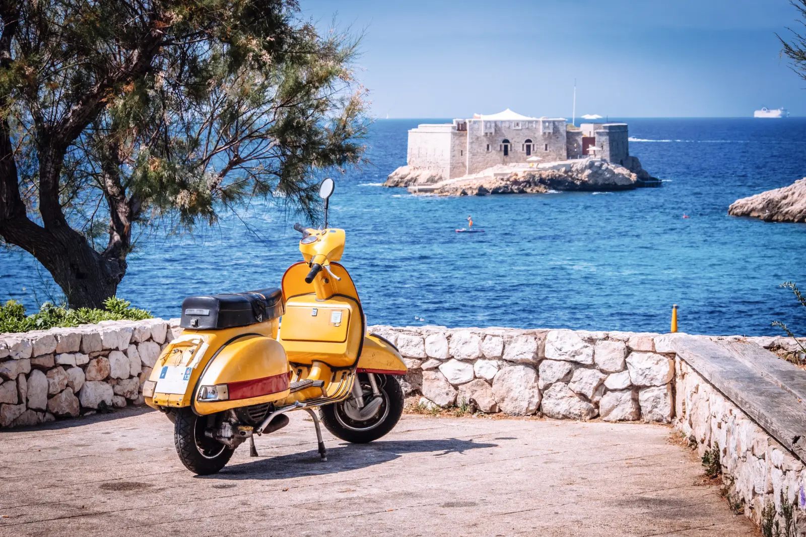 Yellow scooter in front of the sea and an island with a fortress in the background.