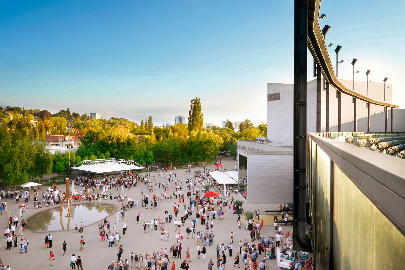 Folla su una piazza accanto a un edificio moderno in una giornata di sole.