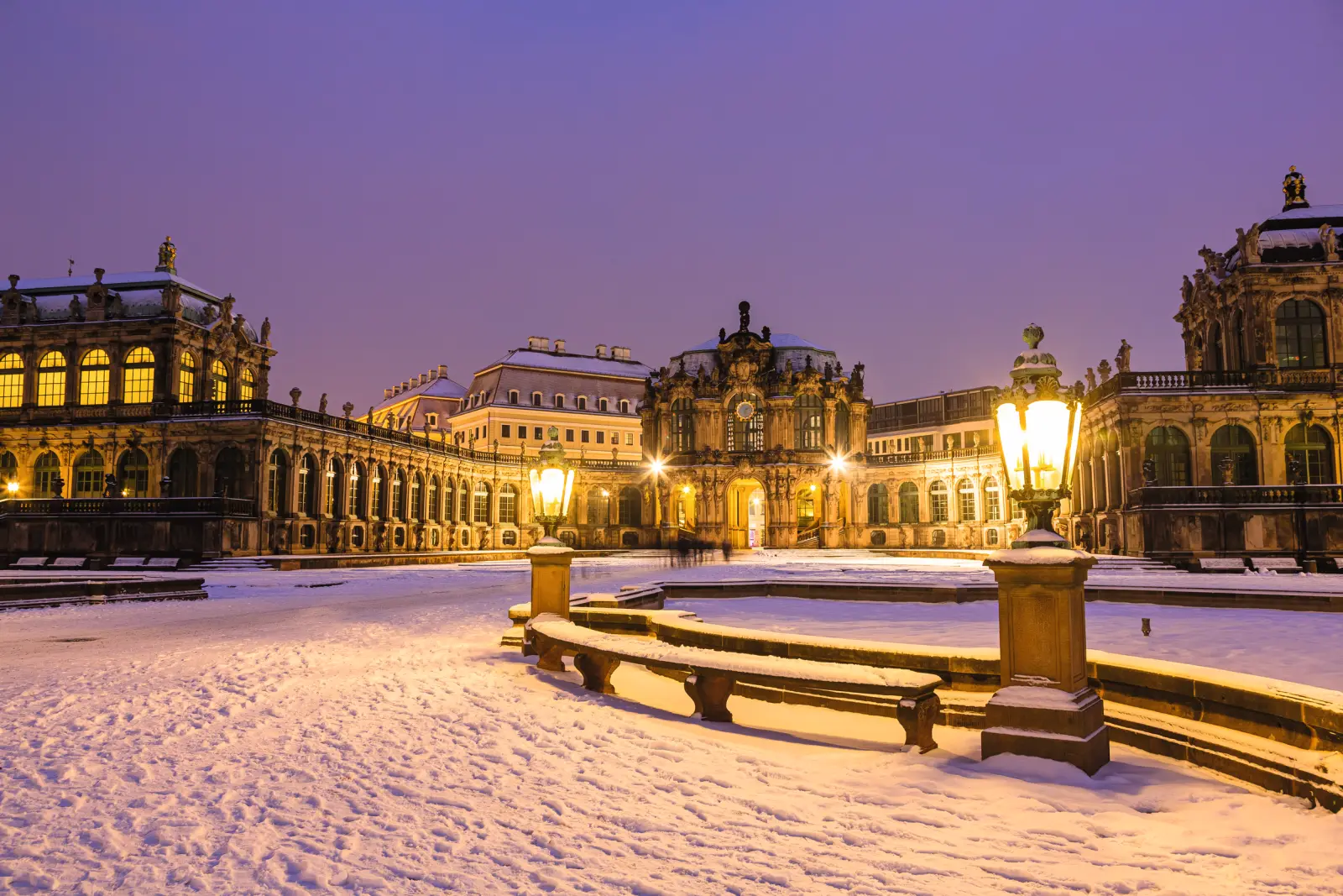 Snow-covered inner courtyard of the Dresden Zwinger at dusk, illuminated.