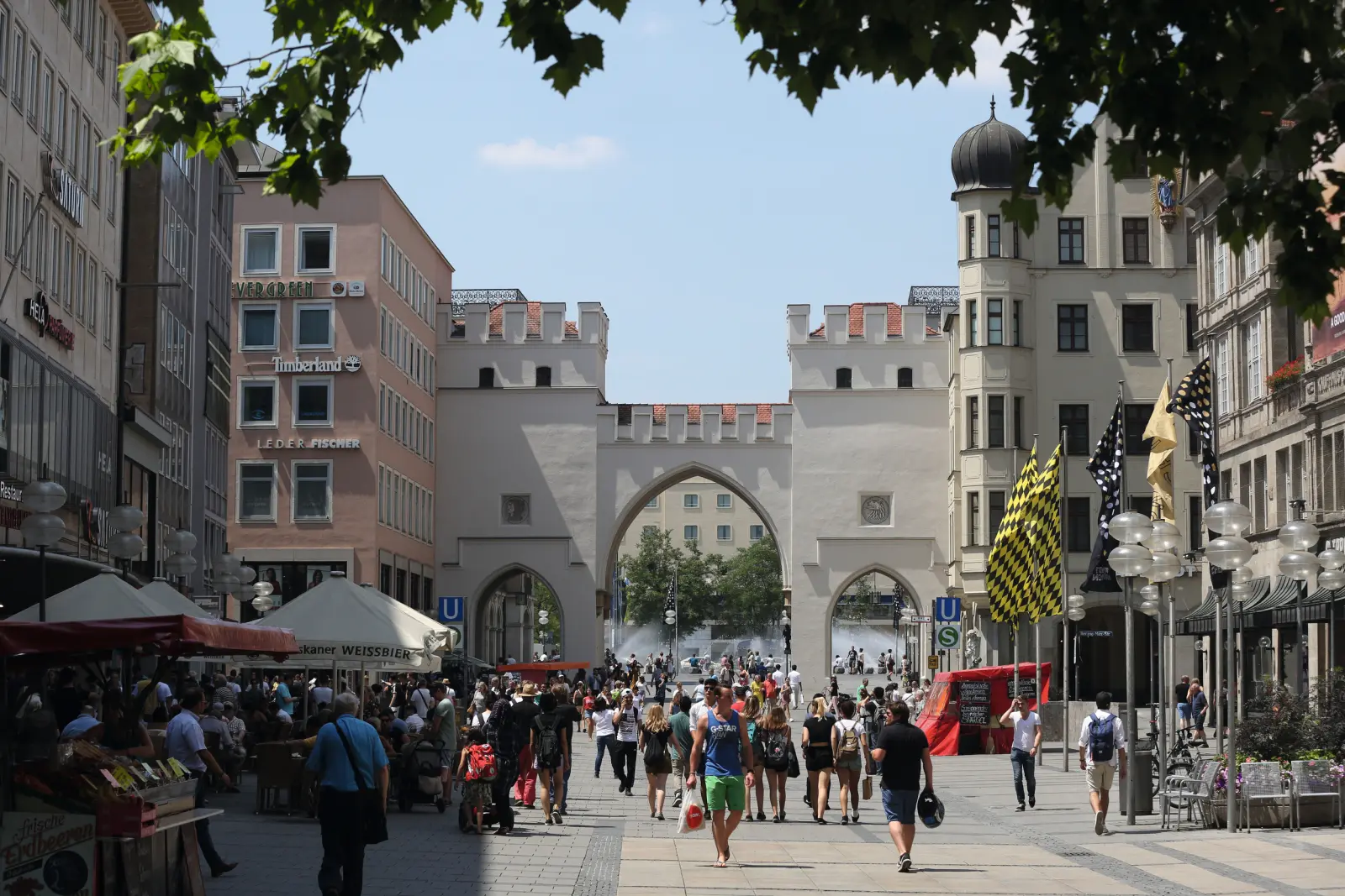 La Karlstor à Munich en été, avec de nombreux passants et des fleurs alentour.
