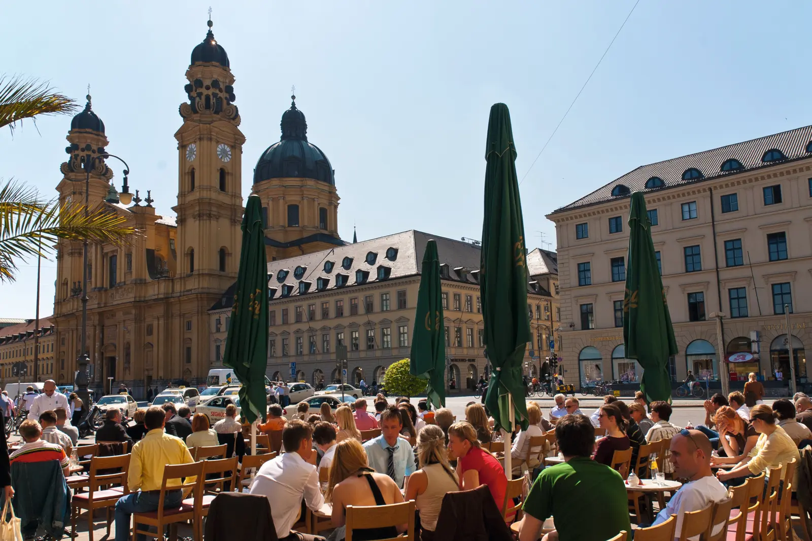 Persone sedute all'aperto in un caffè sull'Odeonsplatz a Monaco di Baviera con tempo soleggiato.