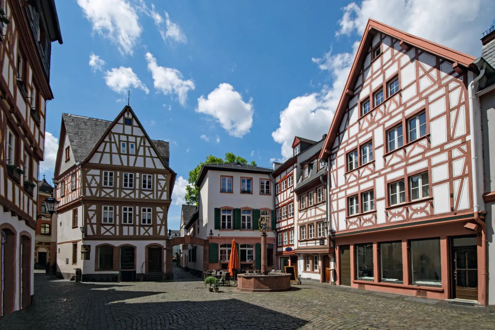 Half-timbered houses on a sunny square with blue sky and clouds.