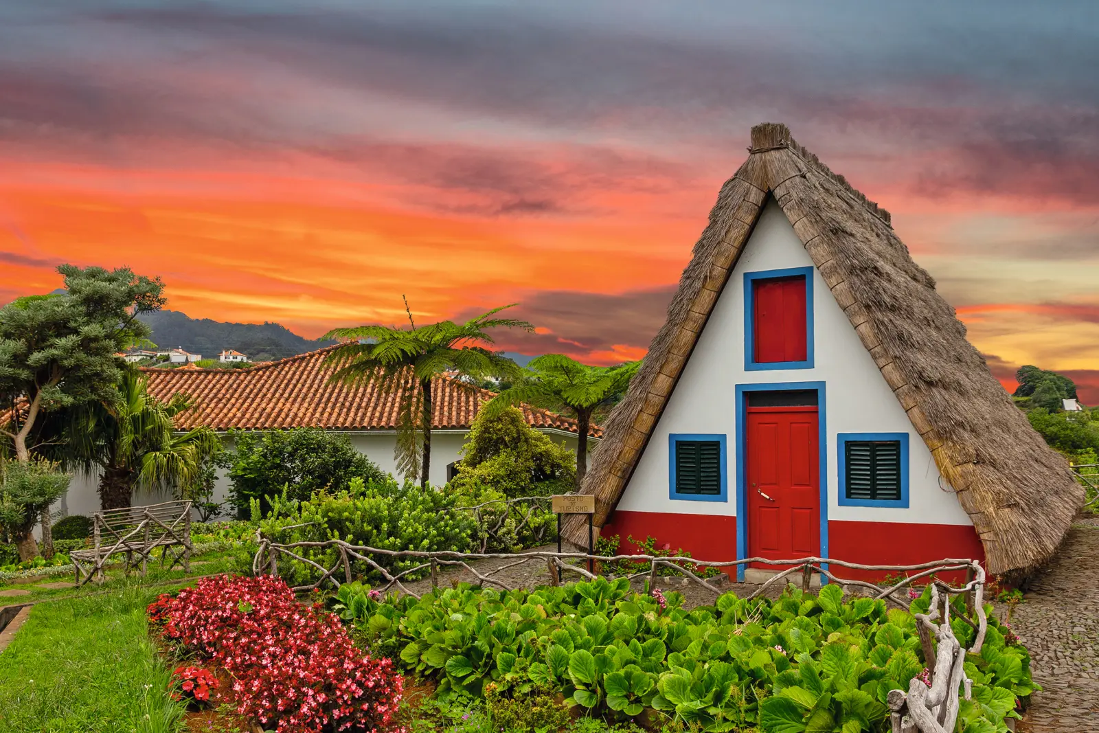 Traditional thatched house against a red sunset sky.