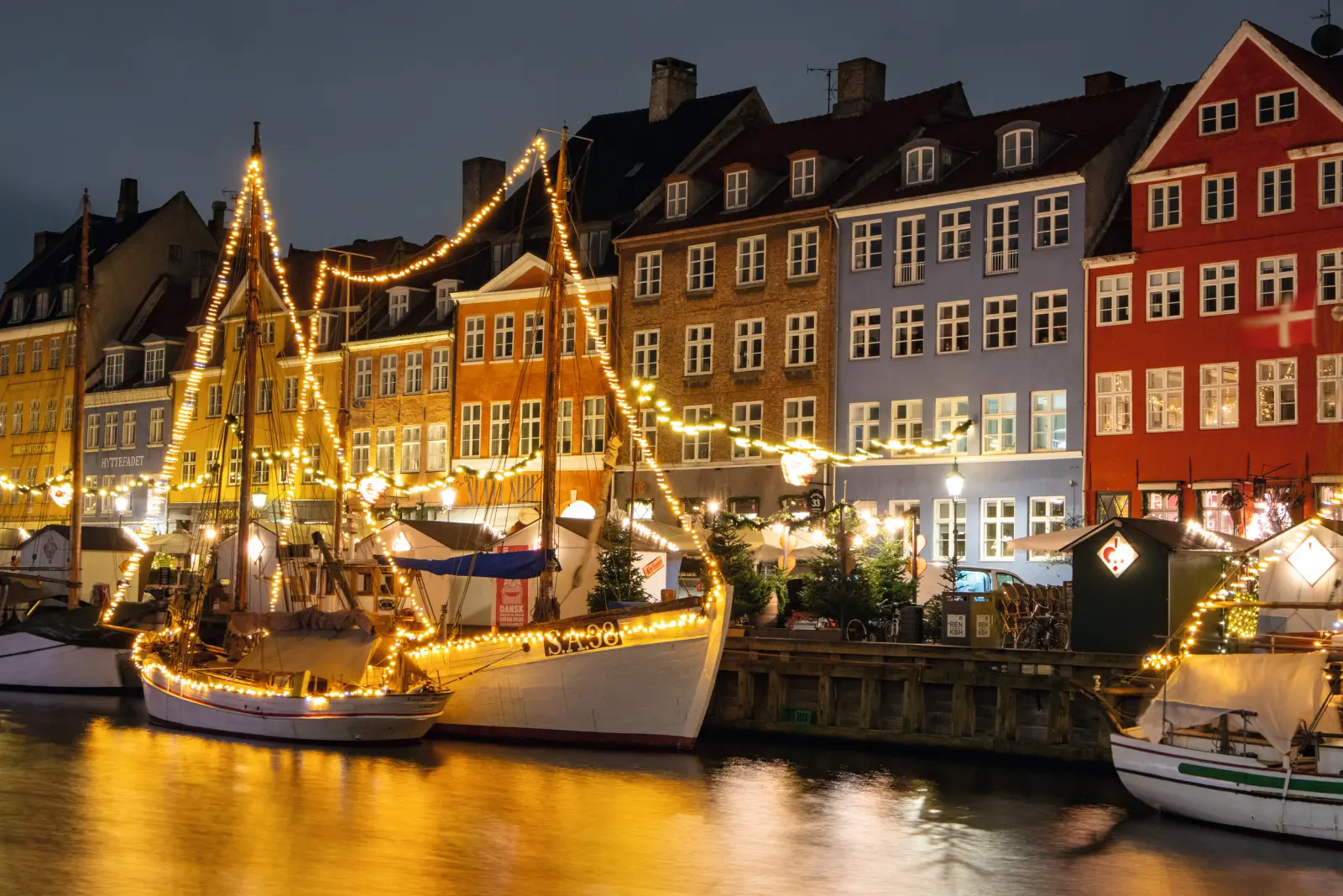Boats decorated with lights and colourful houses on a canal at night.
