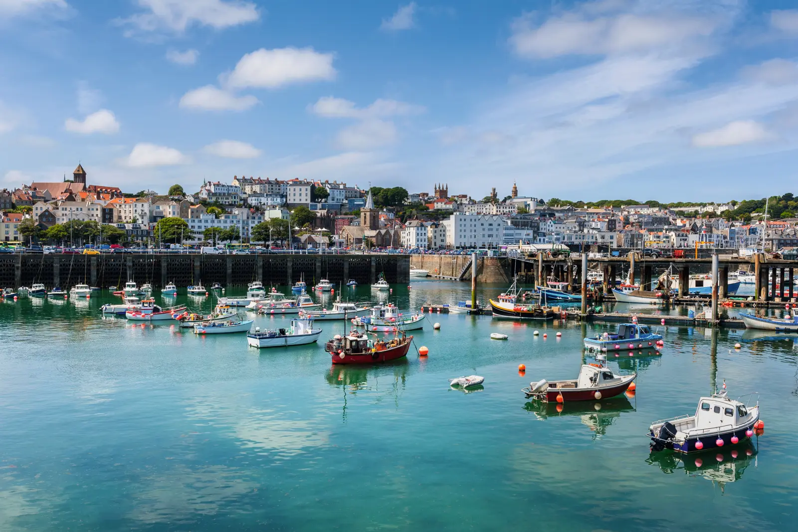 A harbour with fishing boats and a town in the background under a blue sky.