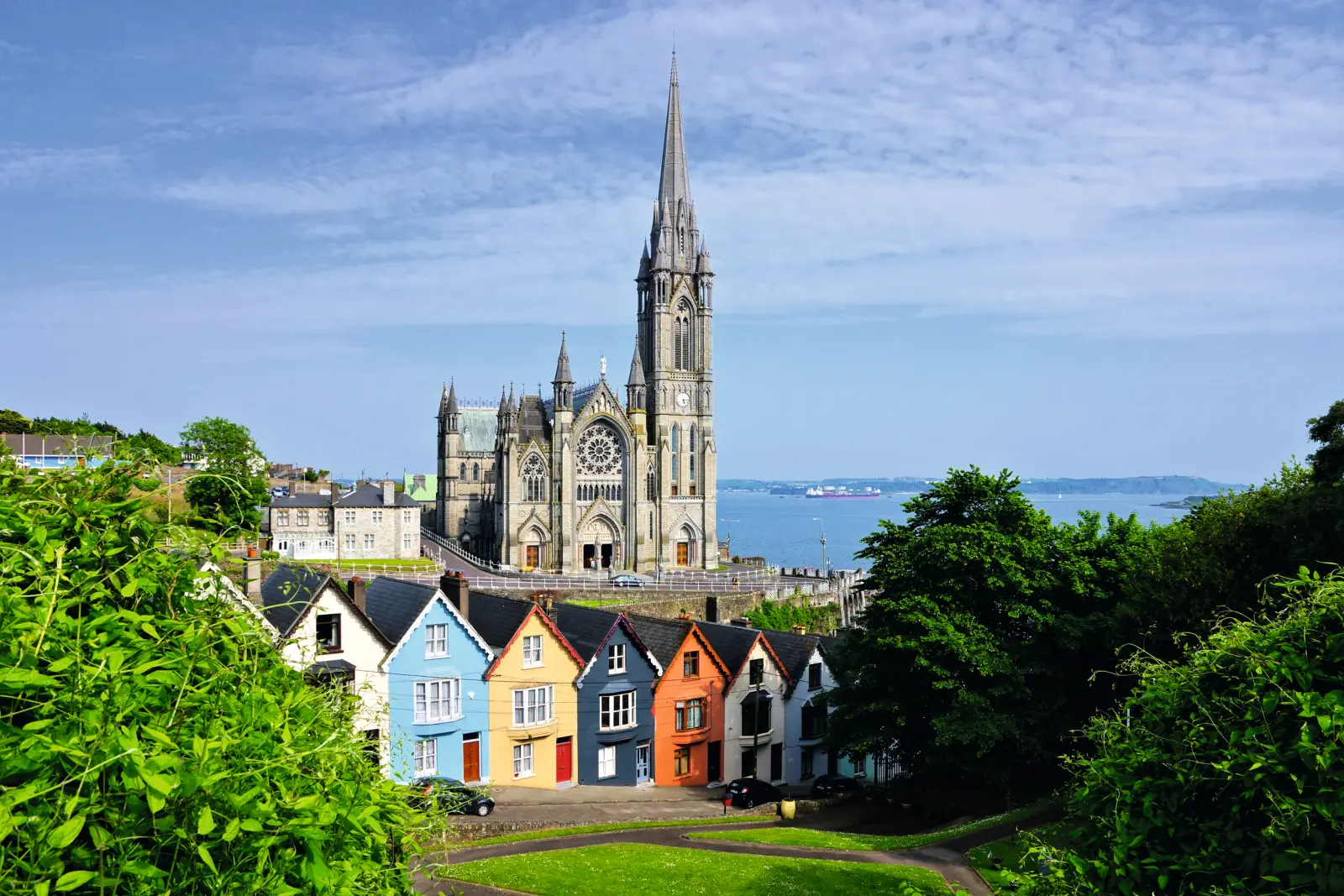 Maisons colorées devant une grande cathédrale, avec la mer à l’arrière-plan.