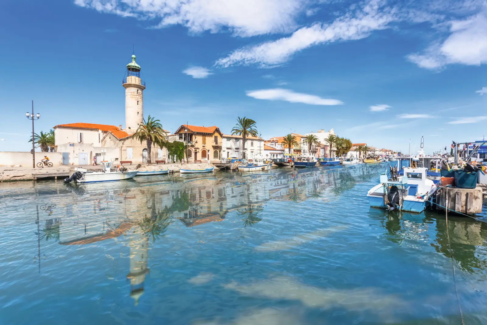 Canal with boats, houses and a lighthouse under a clear sky.