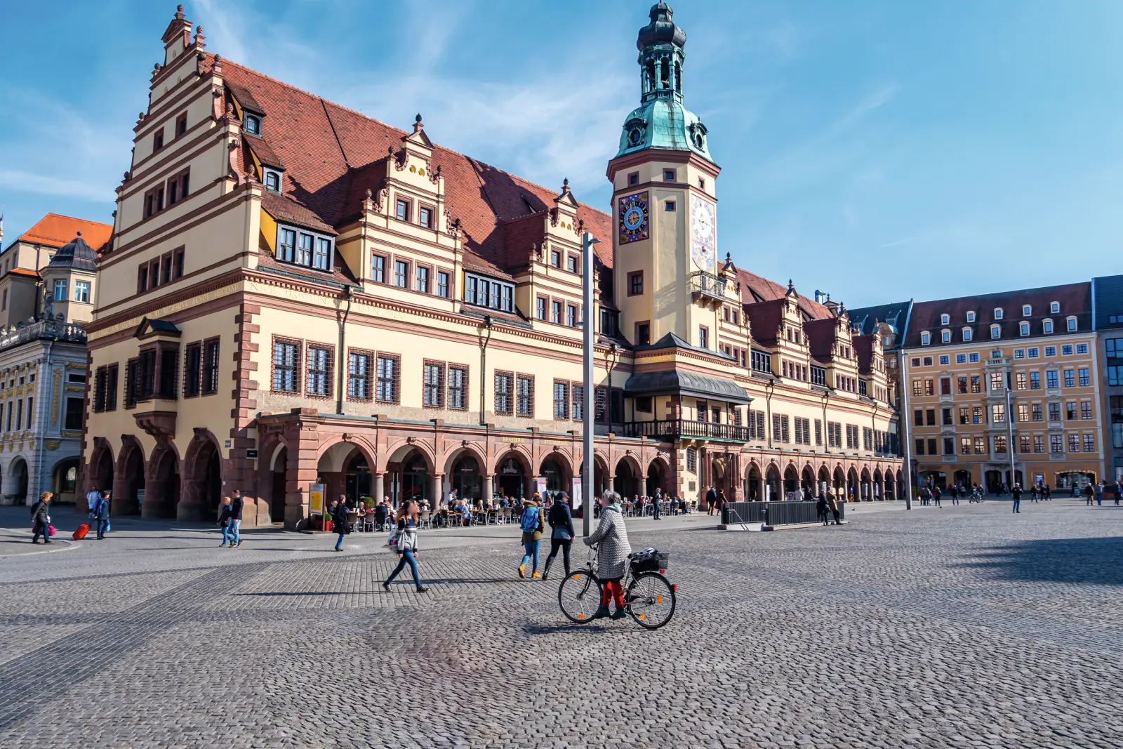 Historisches Gebäude mit Turm auf großem, belebtem Platz bei blauem Himmel.
