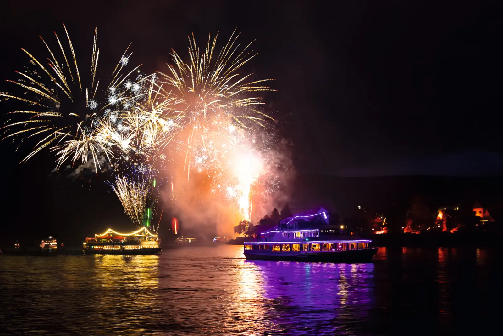 Boats on a river at night with colourful fireworks in the sky.