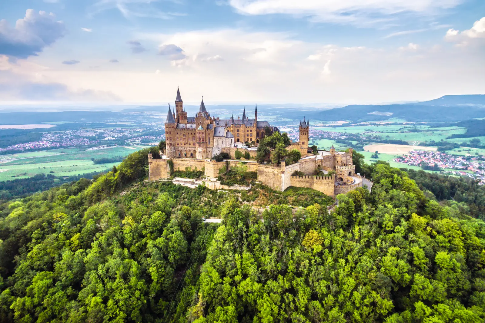 Luftaufnahme einer Burg auf einem bewaldeten Hügel mit umliegender Landschaft.