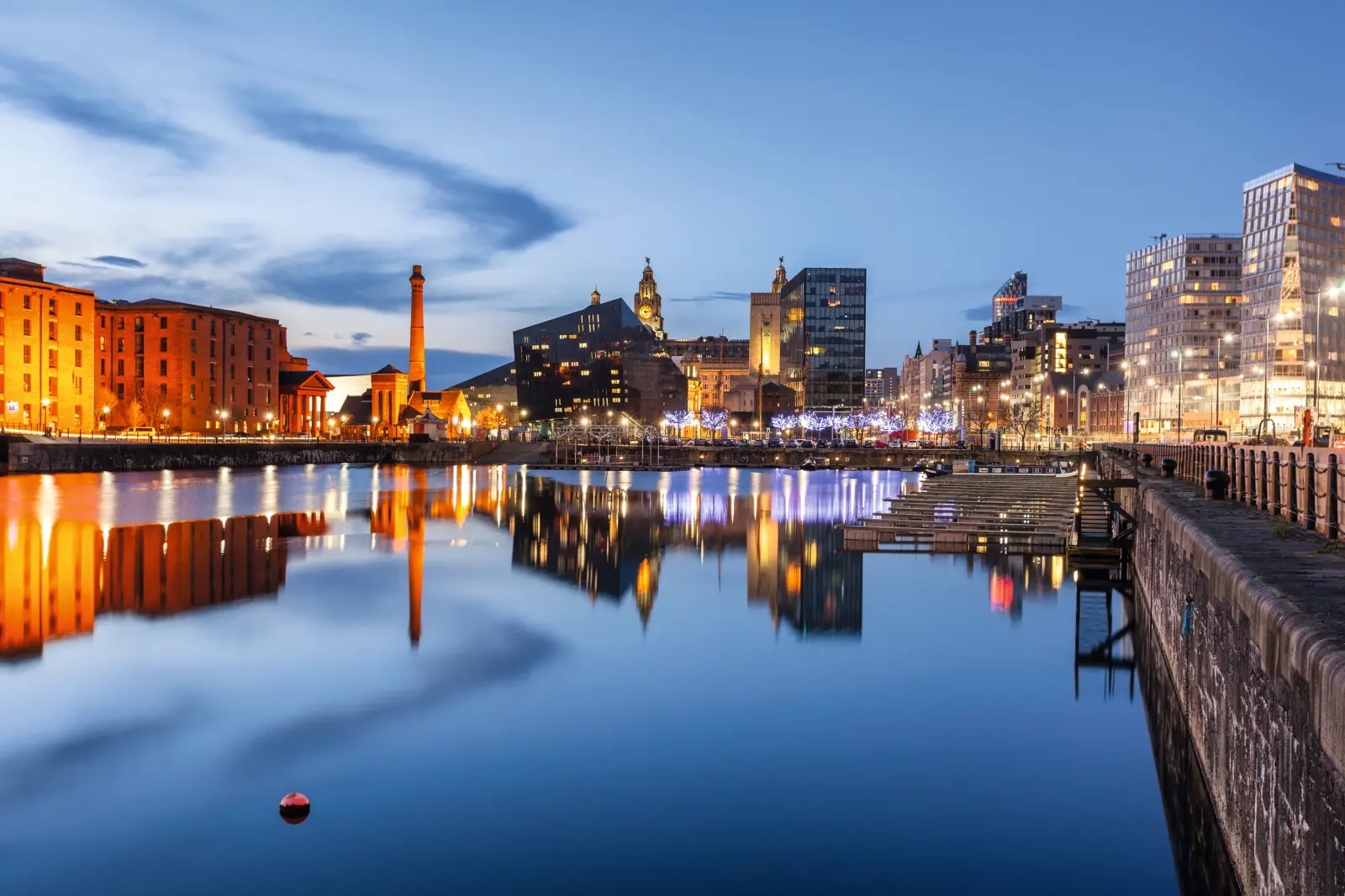 Cityscape at dusk with illuminated buildings along the riverbank.