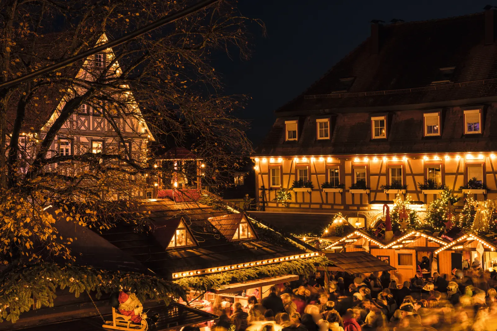 Marché de Noël en soirée avec maisons à colombages et décorations lumineuses.