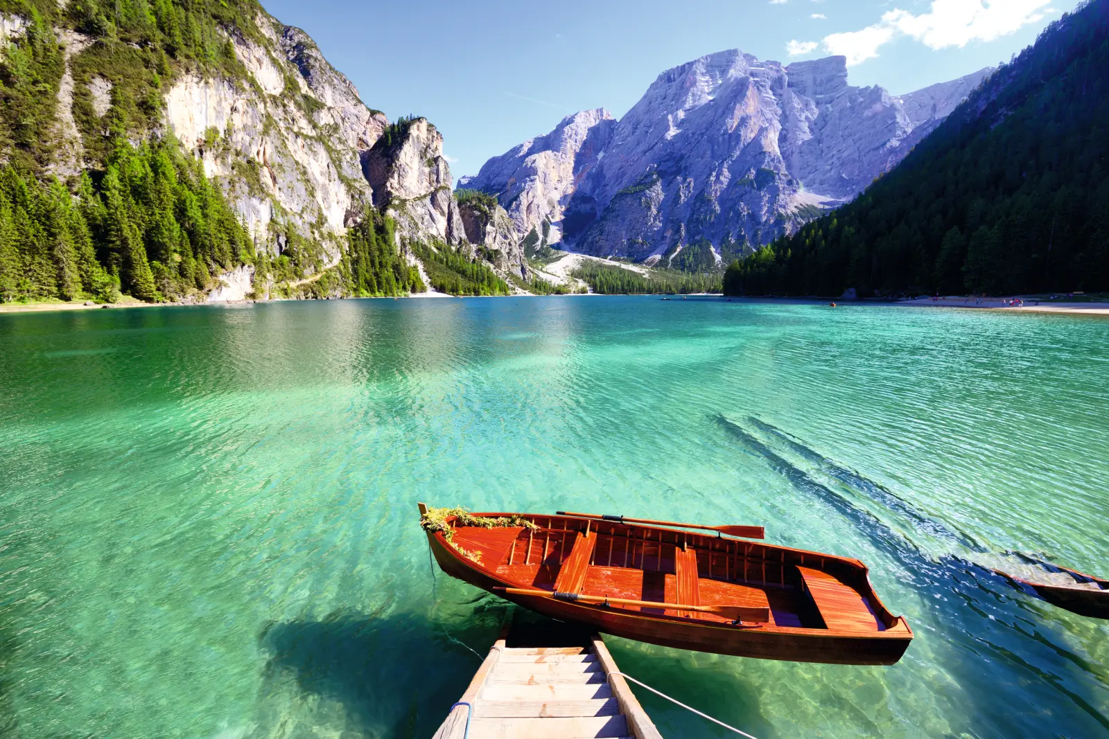 Holzboot auf einem klaren Bergsee, umgeben von Wäldern und hohen Bergen.