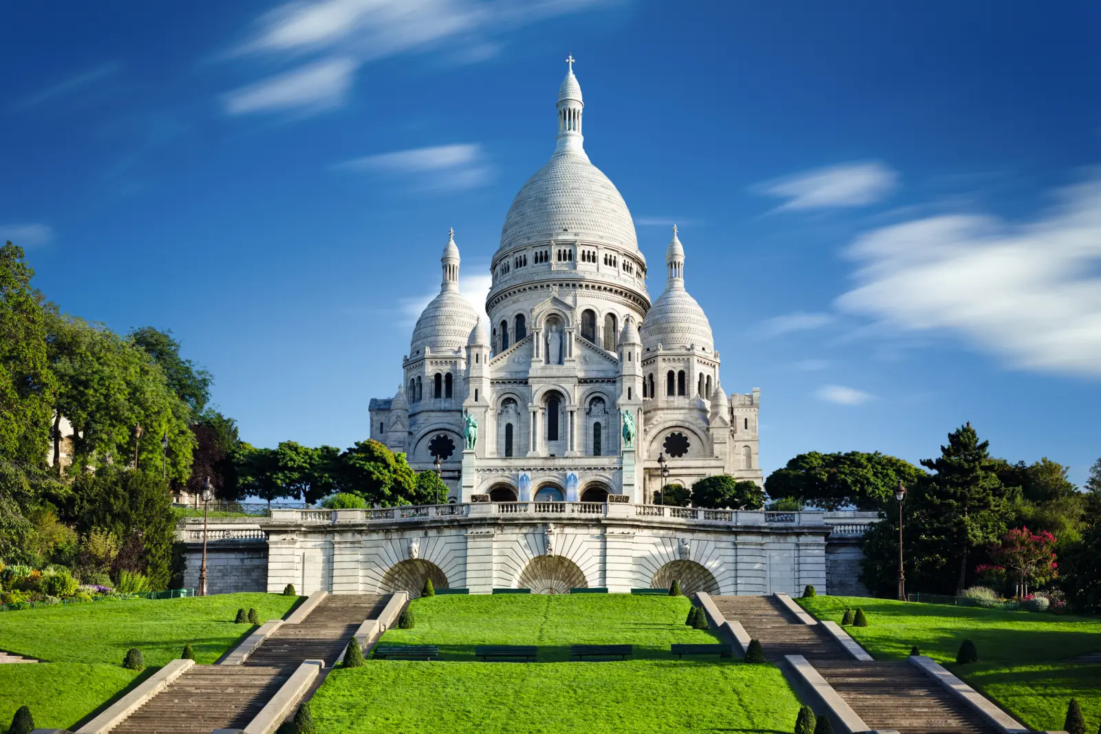 Basilique du Sacré-Cœur à Paris sous un ciel bleu, avec un parc verdoyant et luxuriant.