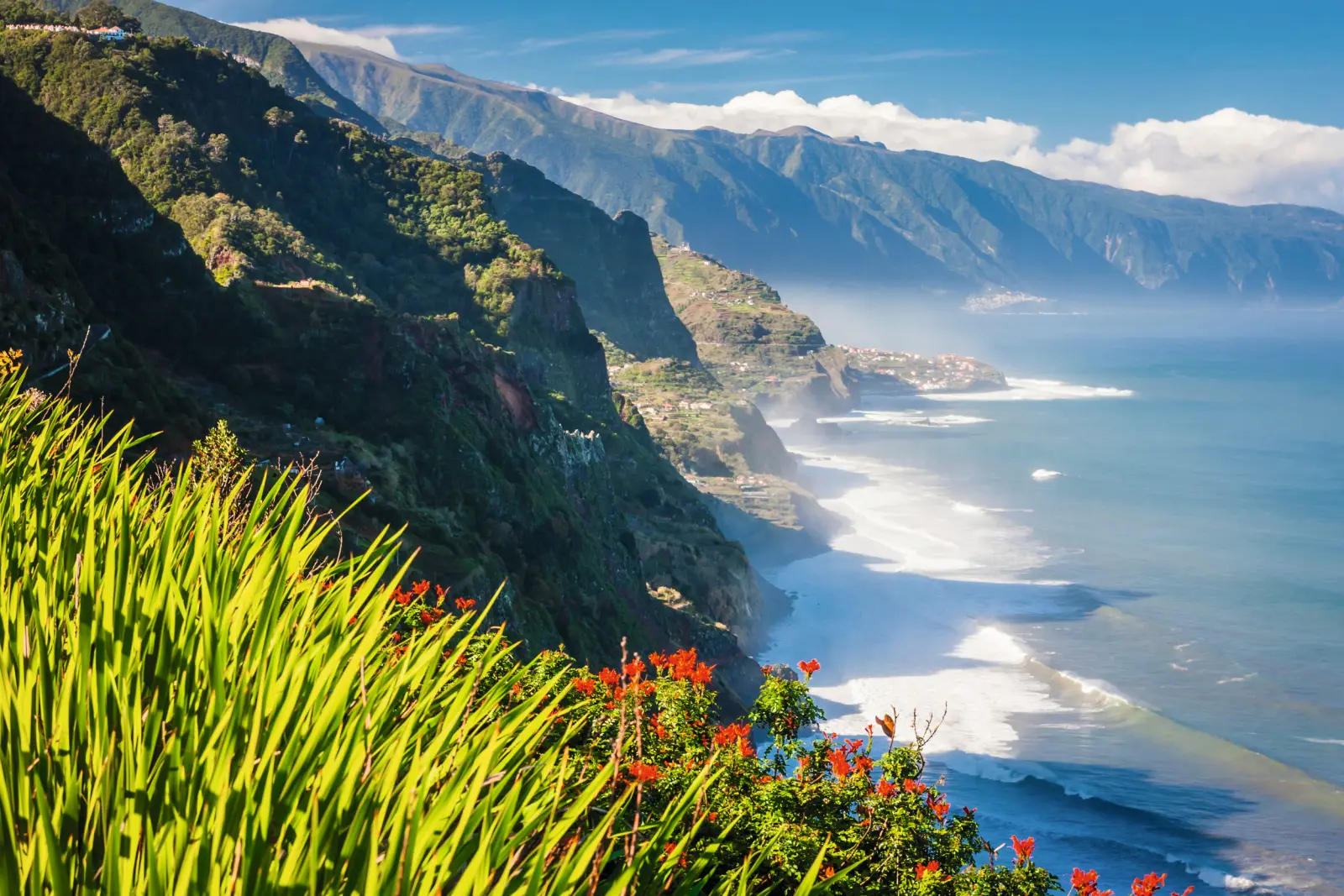 Coastal landscape with mountains, sea and lush vegetation under a blue sky.