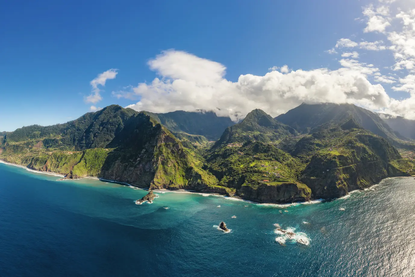 Aerial view of a green island with mountains and clear blue sea.