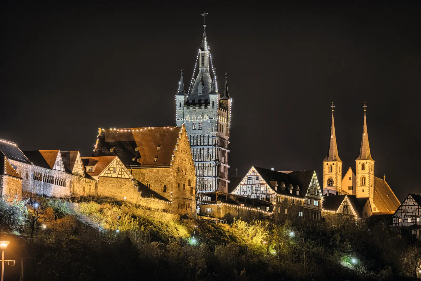 Ensemble de château illuminé de nuit avec tours et maisons à colombages.