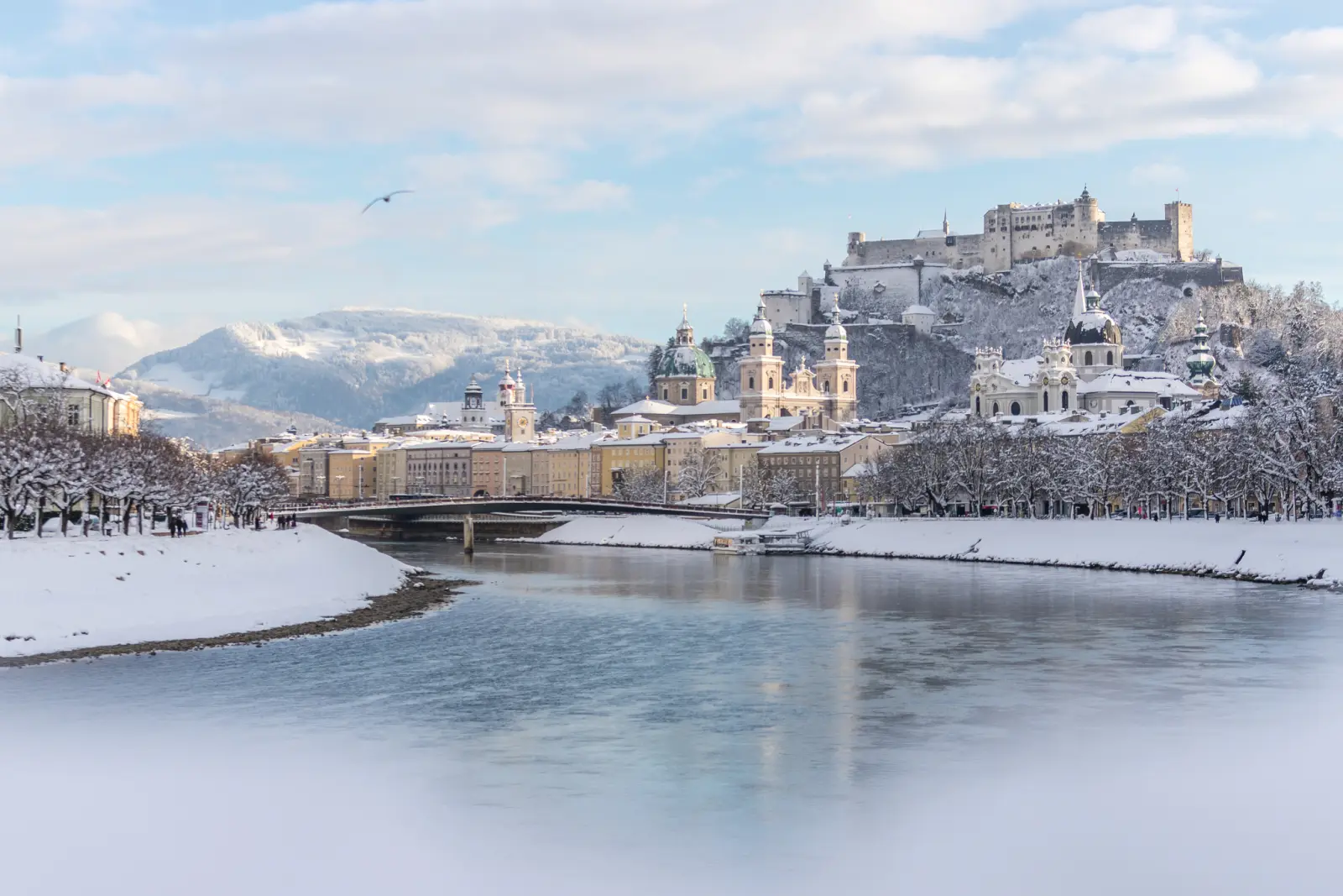 Paesaggio urbano invernale con fiume e castello sullo sfondo.