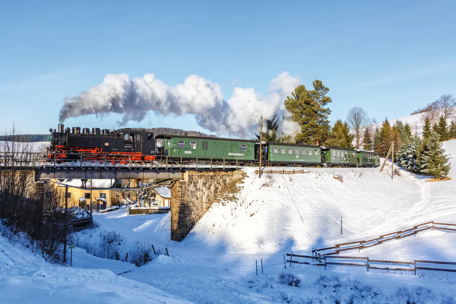 Black steam locomotive on a bridge in a snowy winter landscape.