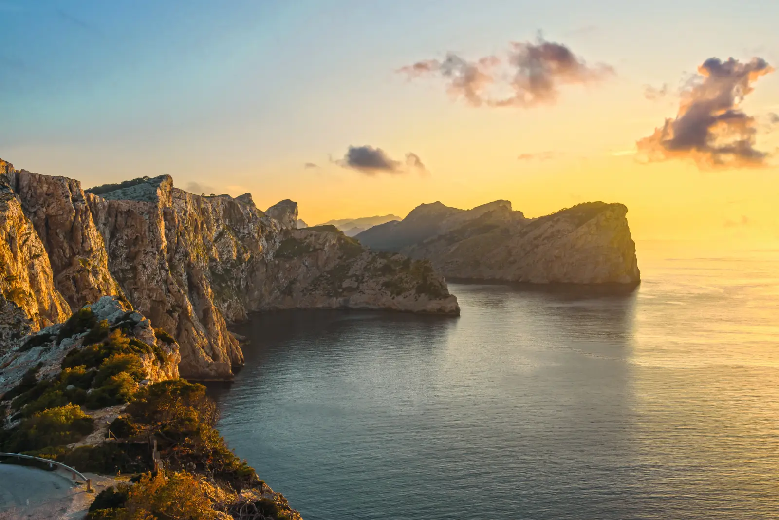 Paesaggio di scogliere al tramonto con mare calmo e nuvole nel cielo.
