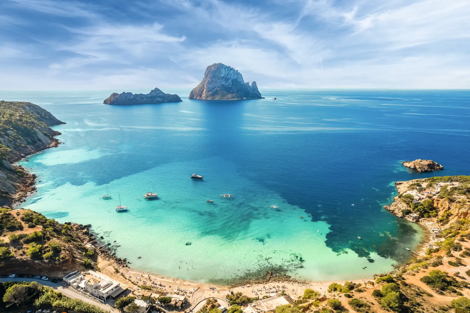 Coastal landscape with clear water and sailing boats, with rocks in the sea in the background