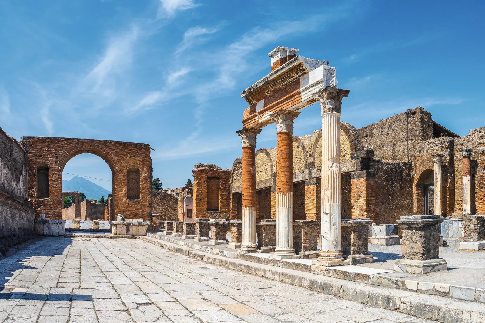 Rovine antiche a Pompei con vista sul Vesuvio e cielo azzurro sullo sfondo.