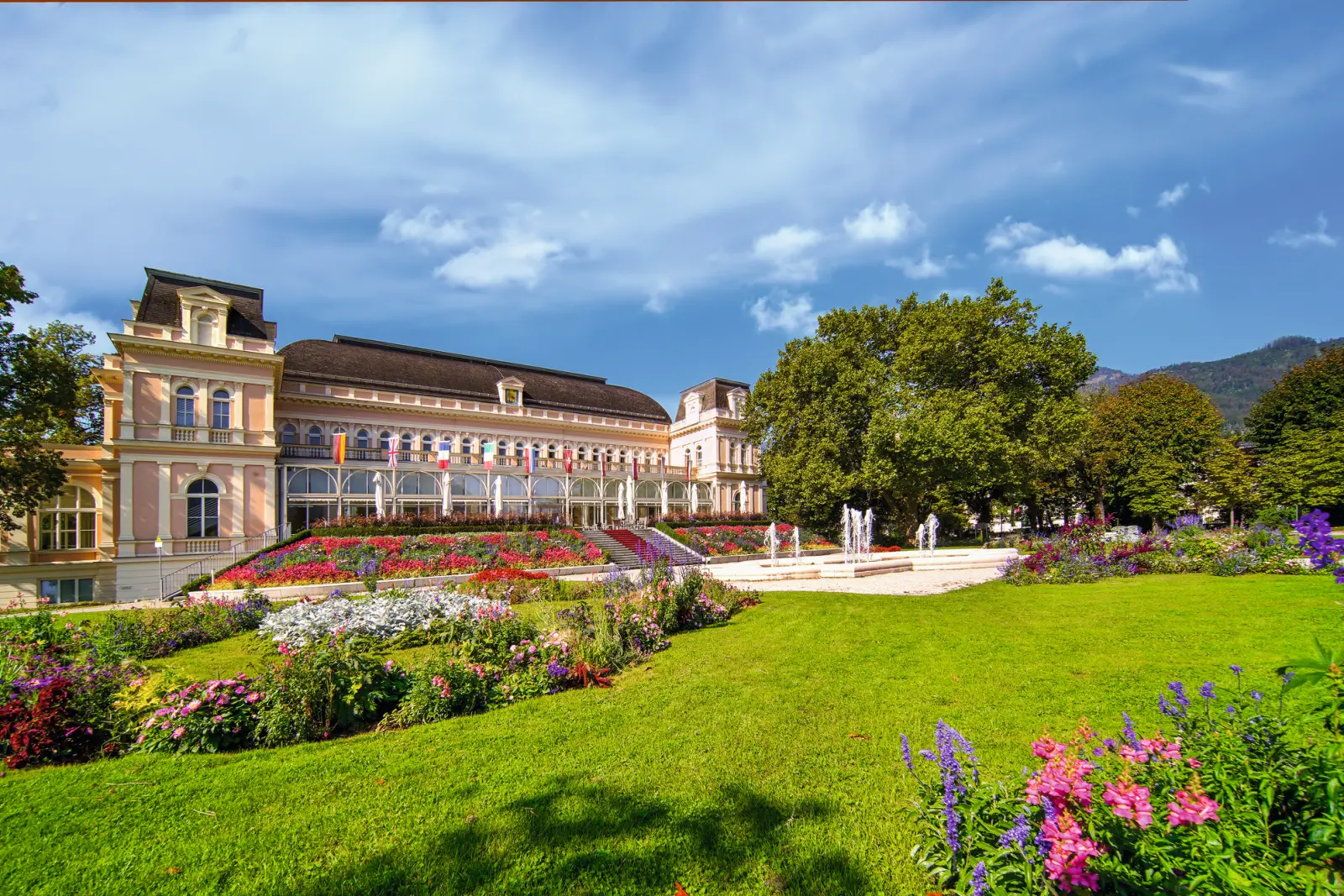 Edificio storico con giardino, fiori colorati e alberi sotto un cielo azzurro.