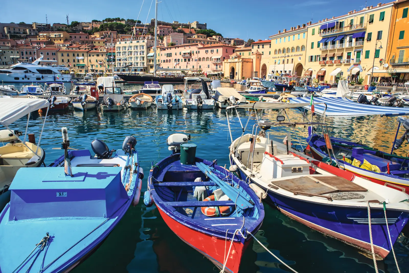 Colourful boats in a Mediterranean harbour in front of historic buildings.