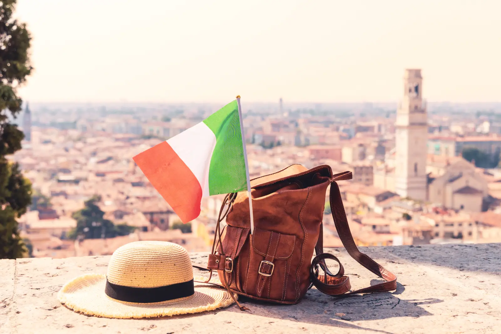 Chapeau, sac à dos et drapeau italien devant un panorama urbain.