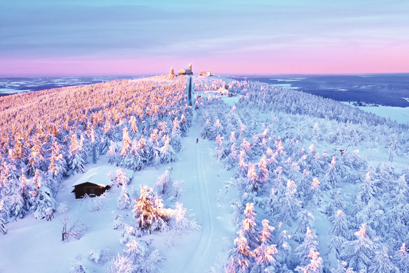Snow-covered landscape with hills and forest in the evening light.