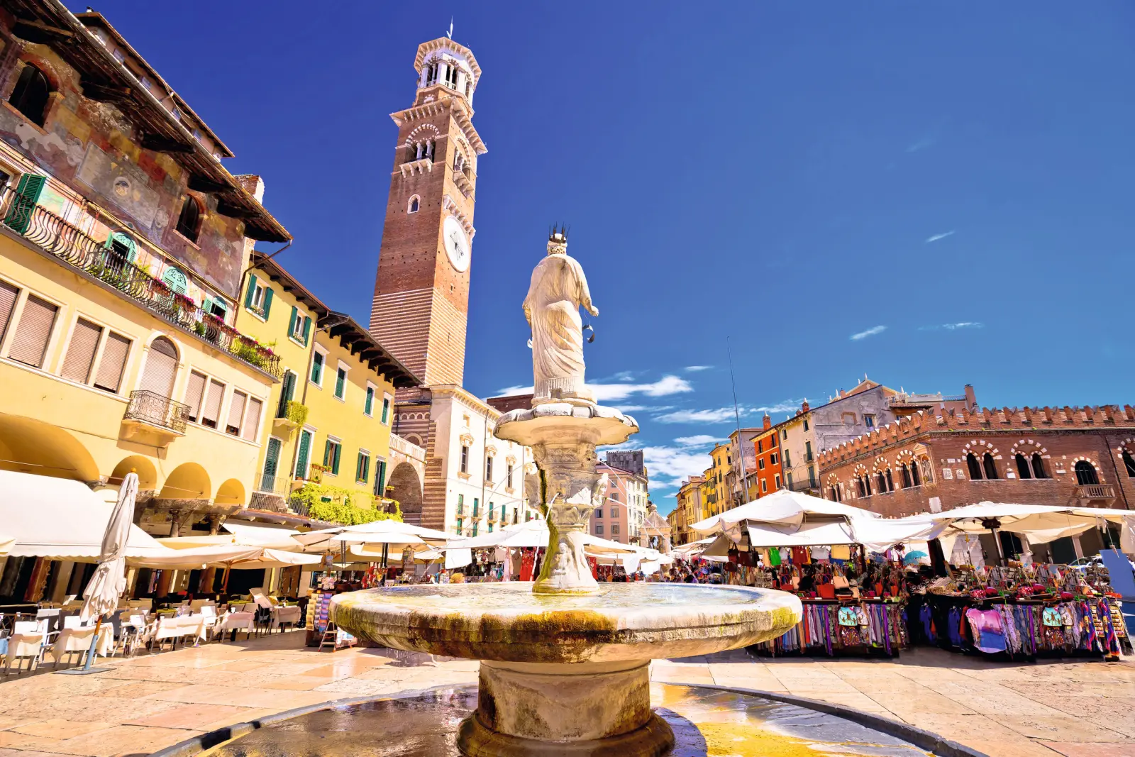 Place du marché avec fontaine et tour de l’horloge par une journée ensoleillée dans une ville européenne.