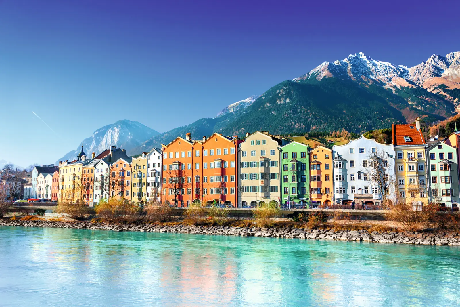 Row of colourful houses by the river with a mountain backdrop.